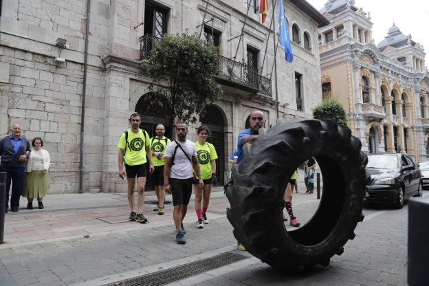 Fran Linares, junto a sus compañeros, empuja la rueda de tractor ante el Consistorio llanisco.