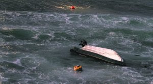 Lancha volcada de la Guardia Civil con sus dos ocupantes a ambos lados de la embarcación aguardando a ser rescatados. :: BORJA IGLESIAS/